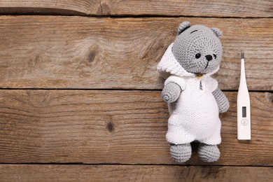 Toy bear and thermometer on wooden background, flat lay. Space for text