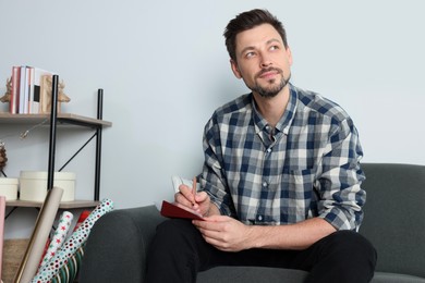 Man writing message in greeting card on sofa in living room