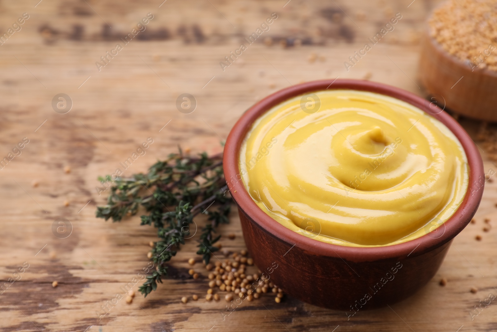 Photo of Delicious mustard, seeds and thyme on wooden table, closeup. Space for text