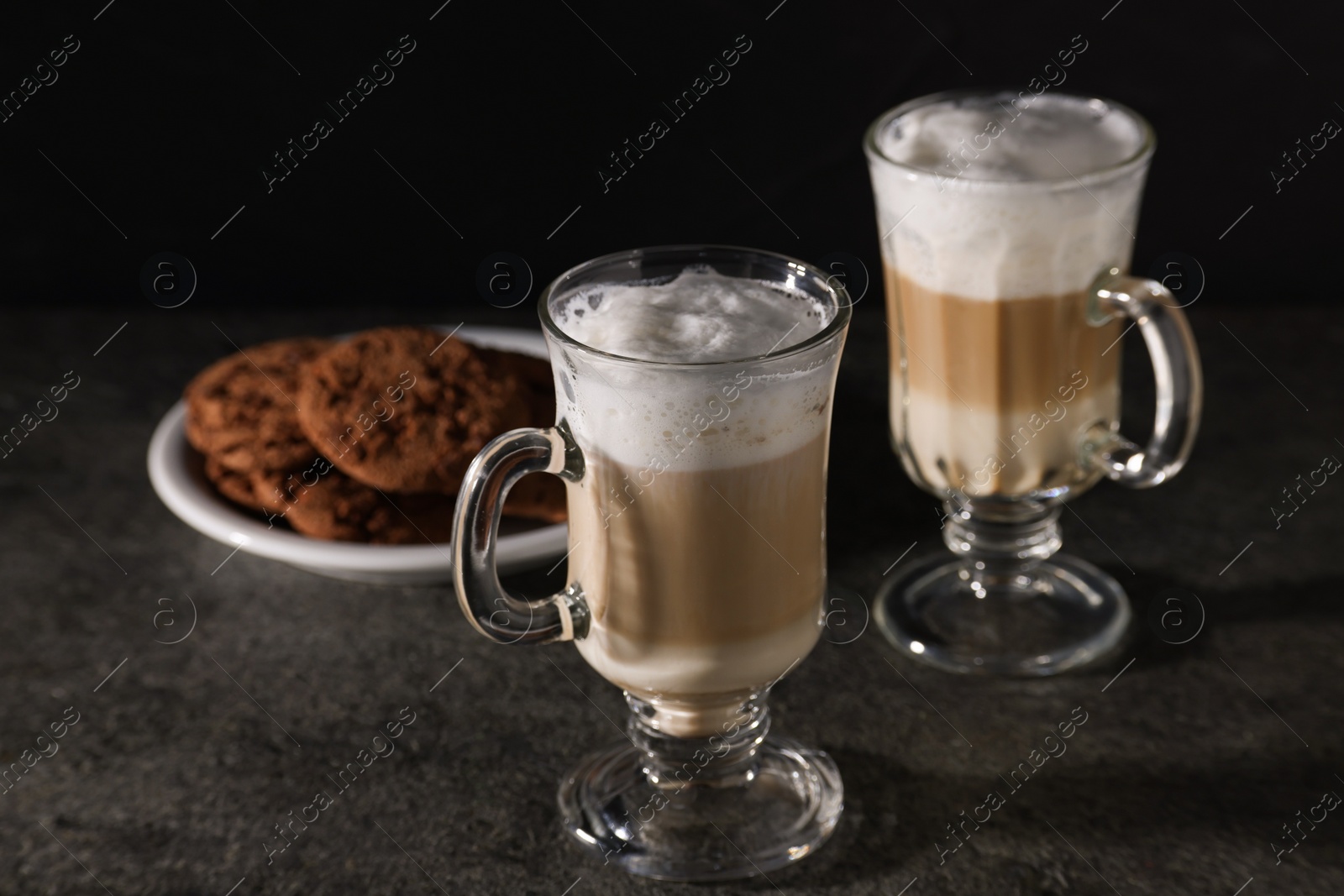 Photo of Aromatic latte macchiato in glasses and chocolate cookies on dark grey table