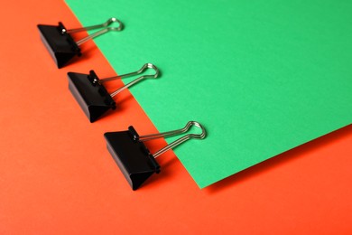 Photo of Black binder clips on color background. Stationery items