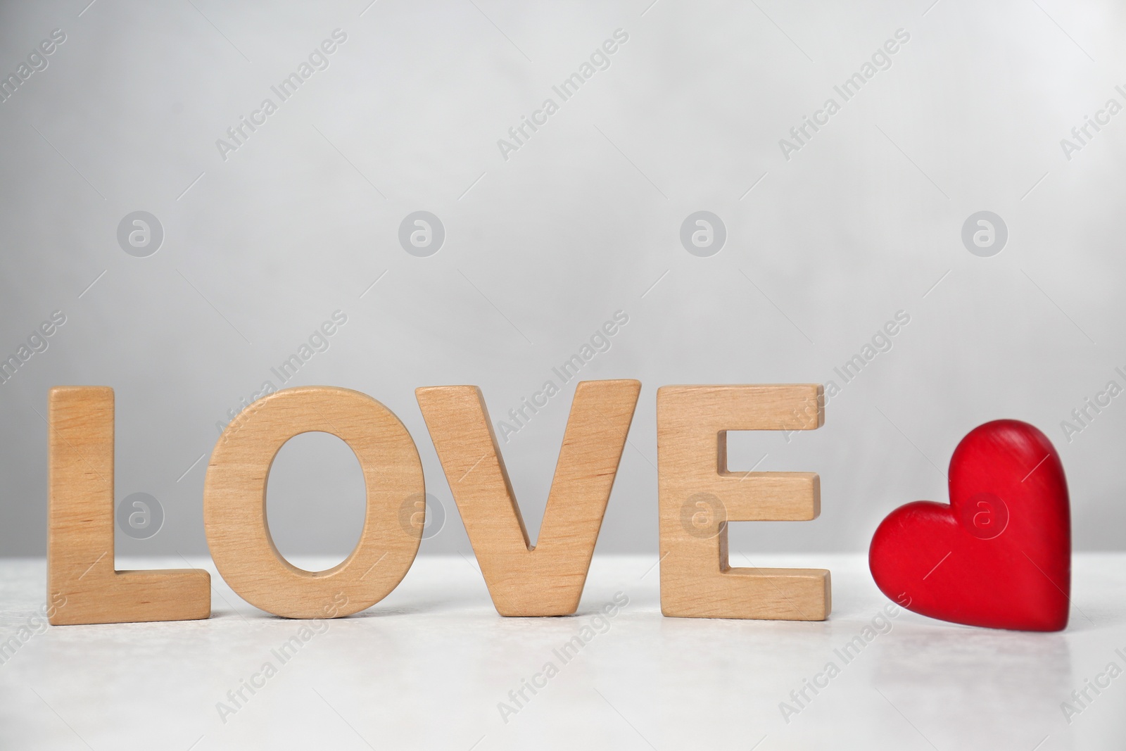 Photo of Word Love made of wooden letters near red decorative heart on light table