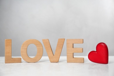 Word Love made of wooden letters near red decorative heart on light table