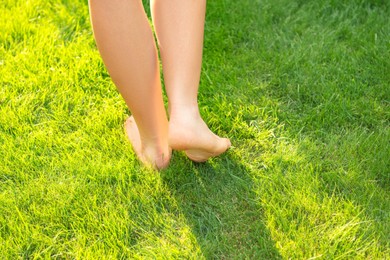 Photo of Teenage girl walking barefoot on green grass outdoors, closeup