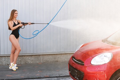 Photo of Young woman in swimsuit with high pressure water jet cleaning automobile at car wash