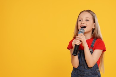Cute little girl with microphone singing on yellow background, space for text
