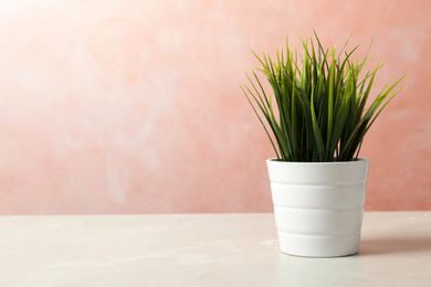 Beautiful artificial plant in flower pot on light table against color background. Space for text