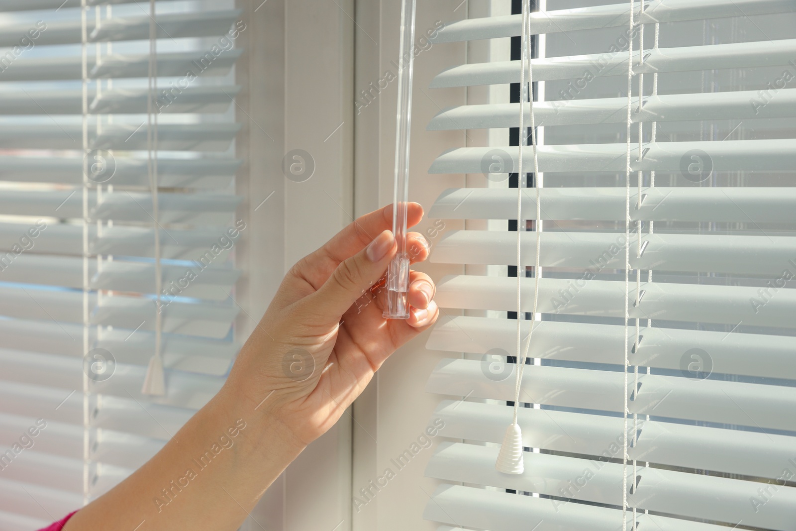 Photo of Woman opening horizontal blinds on window indoors, closeup