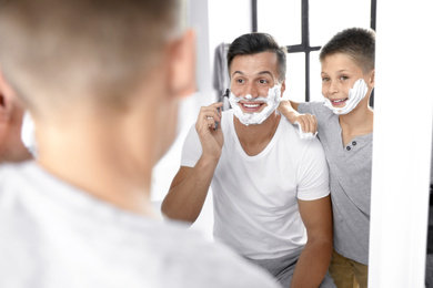Photo of Dad showing his son how to shave near mirror in bathroom