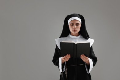 Photo of Nun reading Bible on grey background, space for text