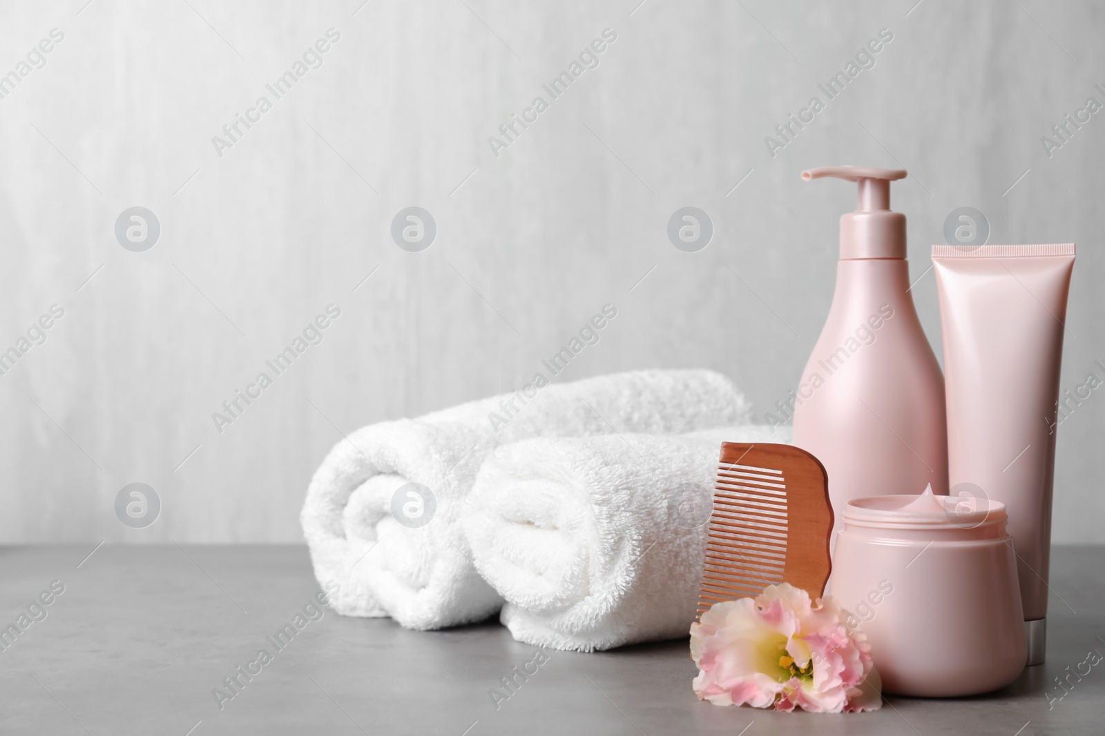 Photo of Different hair products, rolled towels and wooden comb on grey table