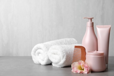 Different hair products, rolled towels and wooden comb on grey table