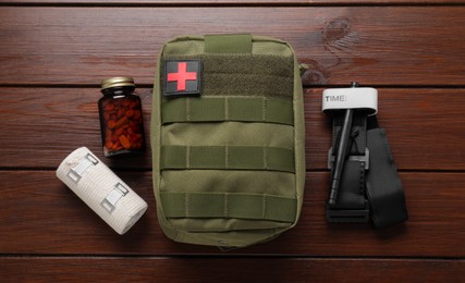 Military first aid kit, tourniquet, pills and elastic bandage on wooden table, flat lay