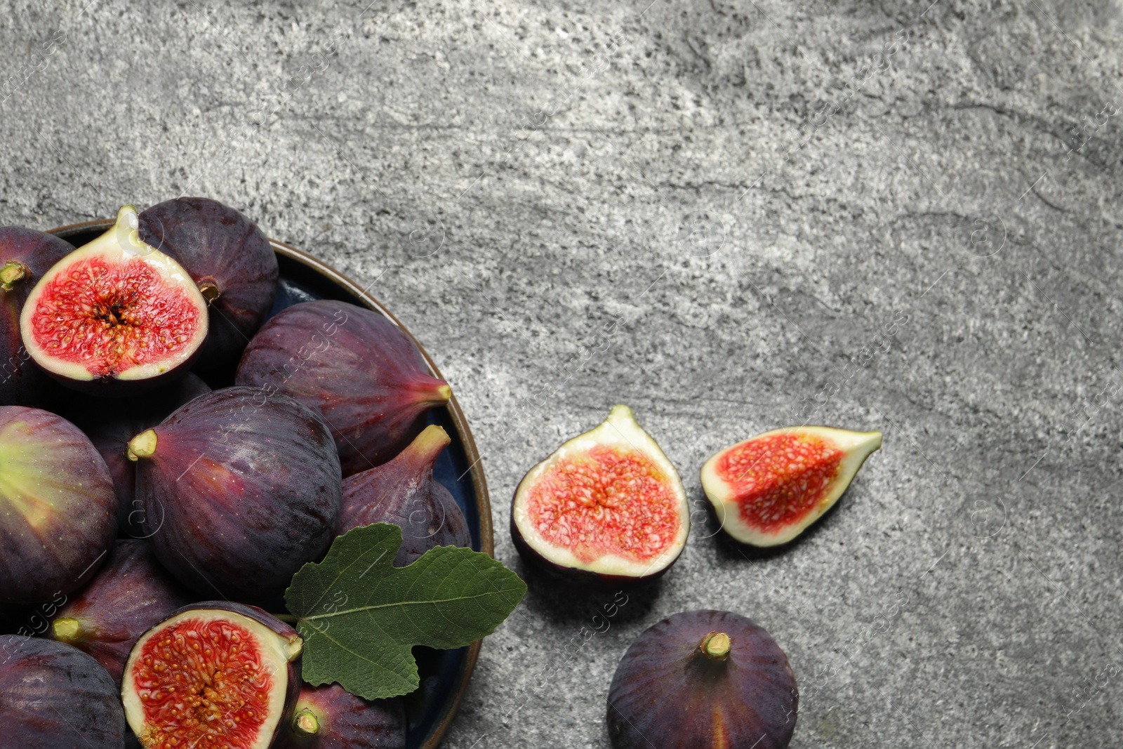 Photo of Whole and cut ripe figs with leaf on light grey textured table, flat lay. Space for text