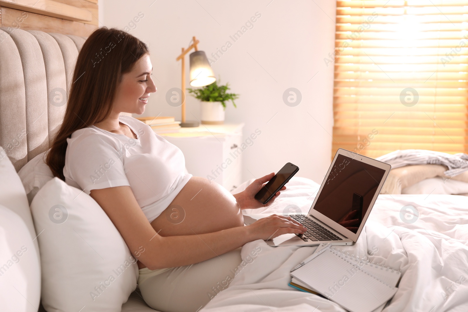 Photo of Pregnant woman working on bed at home. Maternity leave