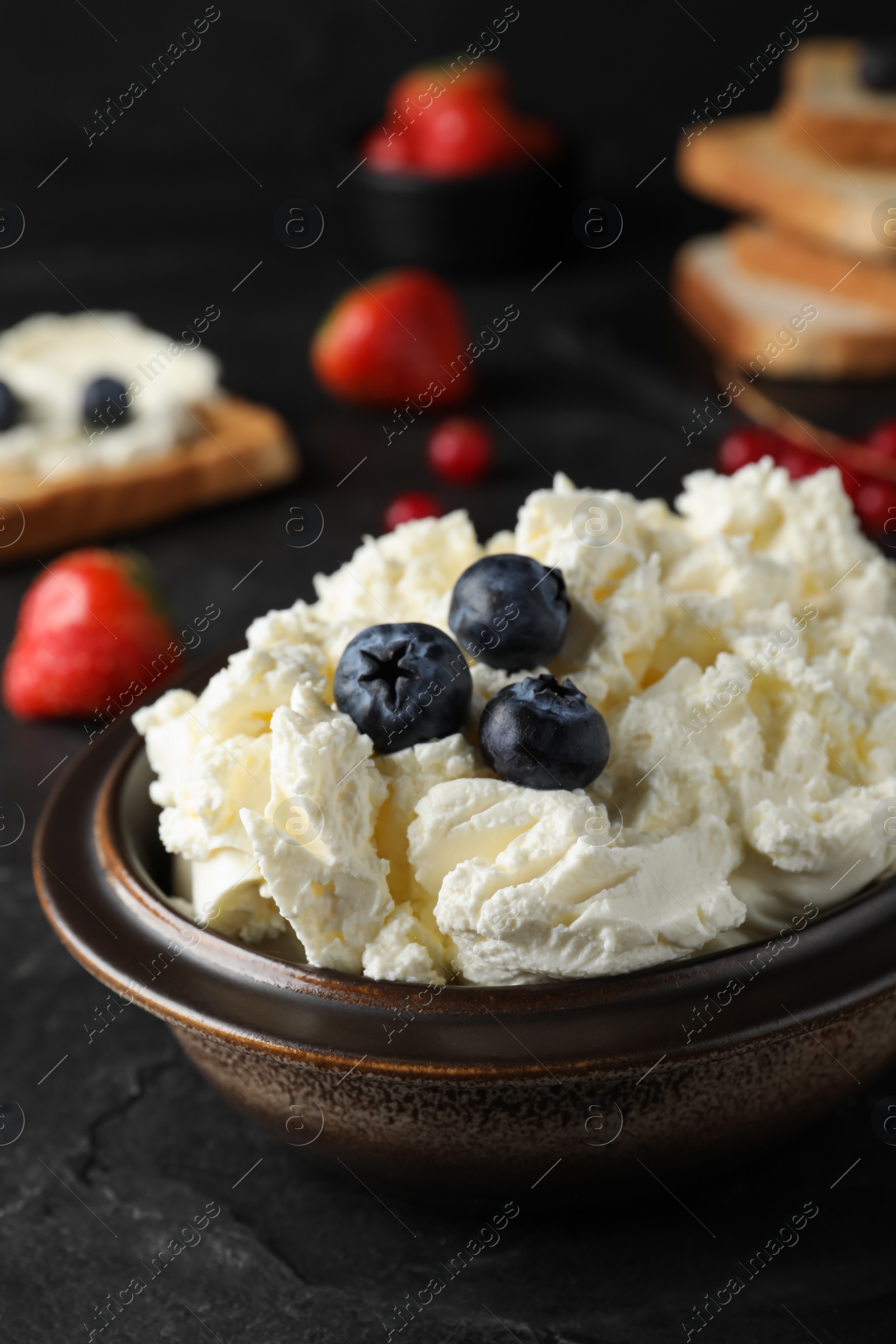 Photo of Tasty cream cheese and fresh berries on black table