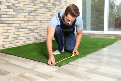 Photo of Man in uniform measuring artificial grass carpet indoors