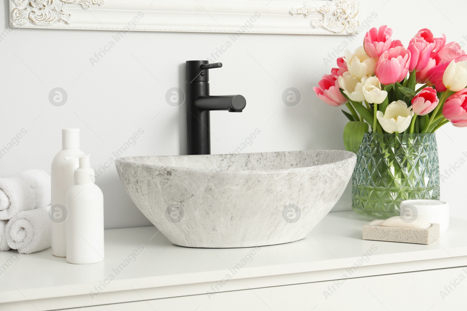 Photo of Vase with beautiful pink tulips and toiletries near sink in bathroom