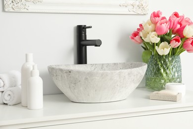 Vase with beautiful pink tulips and toiletries near sink in bathroom