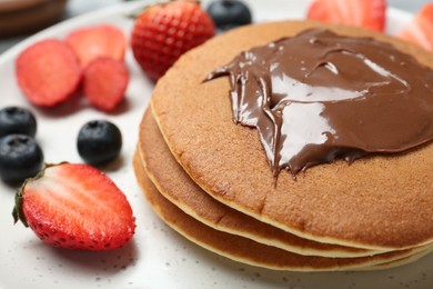 Photo of Tasty pancakes with chocolate paste and berries on plate, closeup