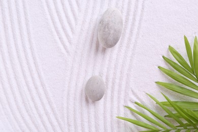 Photo of Zen garden stones and green leaves on white sand with pattern, flat lay