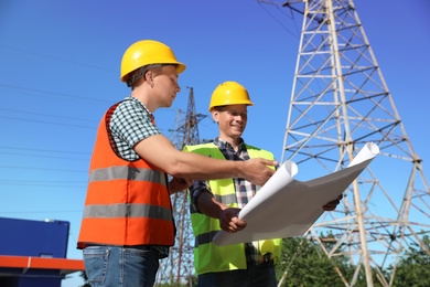 Professional electricians with drafting near high voltage tower