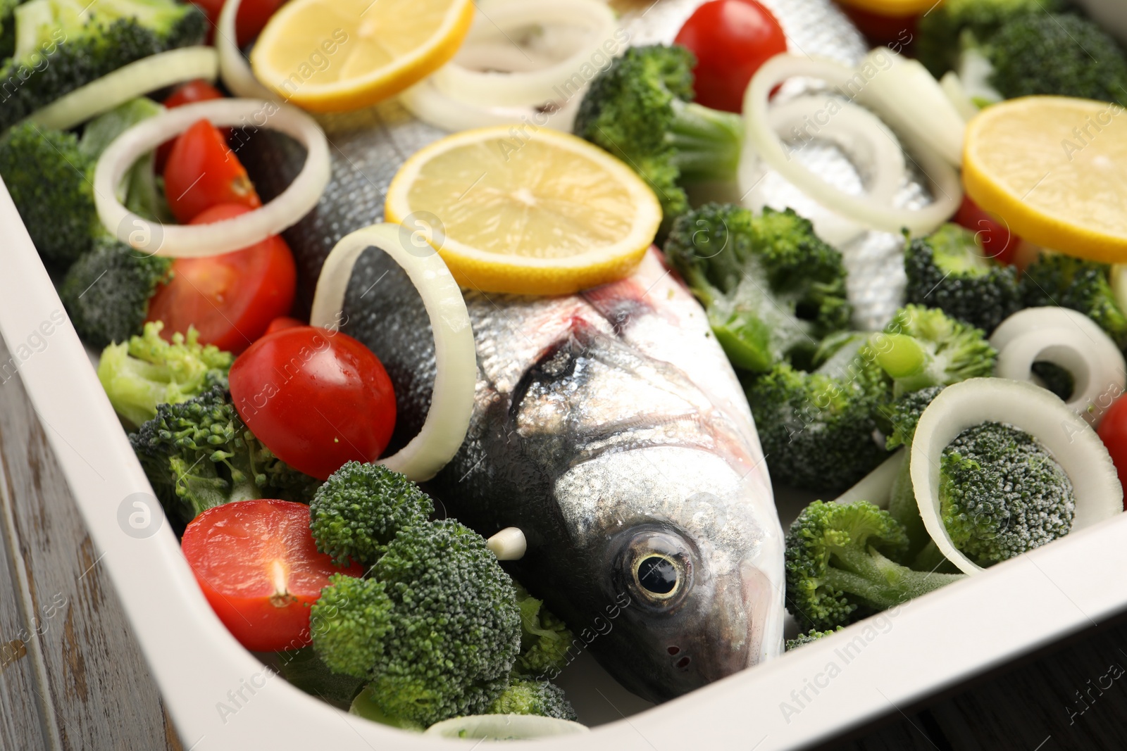 Photo of Raw fish with vegetables and lemon in baking dish on table, closeup