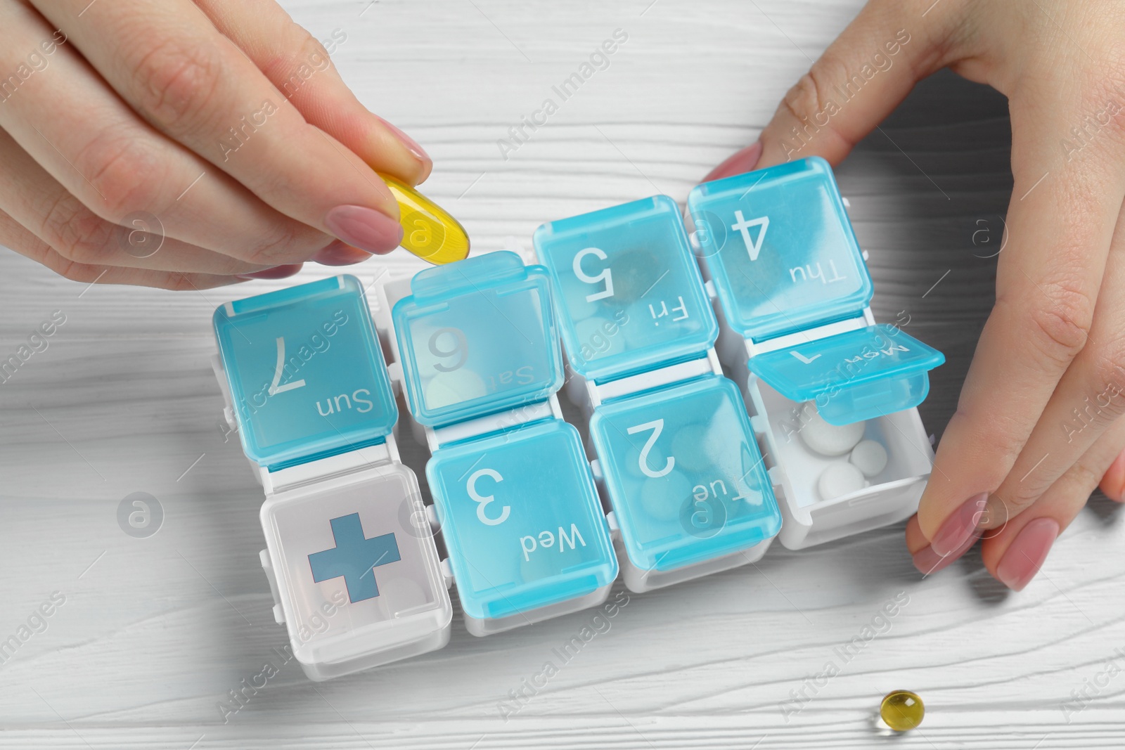 Photo of Woman putting pill into weekly organizer at wooden white table, top view