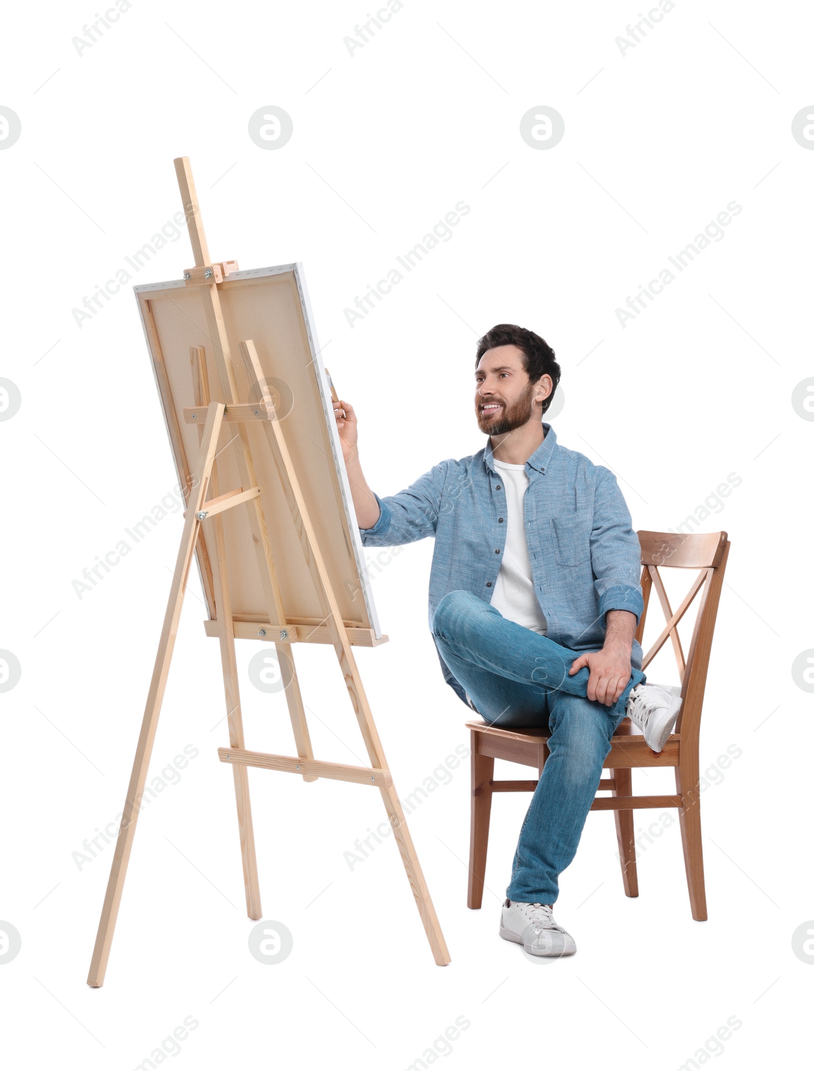 Photo of Happy man painting with brush against white background. Using easel to hold canvas