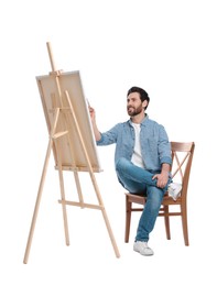 Photo of Happy man painting with brush against white background. Using easel to hold canvas