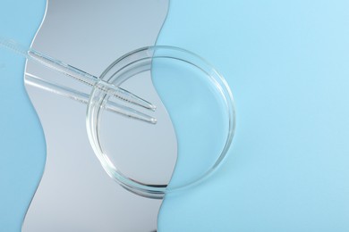 Photo of Empty petri dish, pipette and mirror on light blue background, flat lay. Space for text