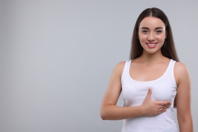 Beautiful young woman doing breast self-examination on light grey background, space for text