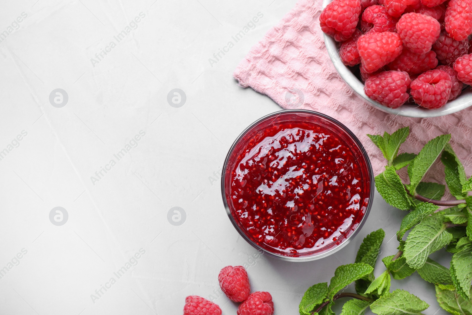 Photo of Delicious jam and fresh raspberries on grey table, flat lay. Space for text
