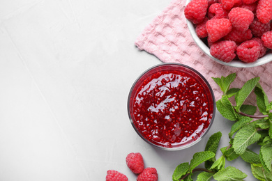 Photo of Delicious jam and fresh raspberries on grey table, flat lay. Space for text