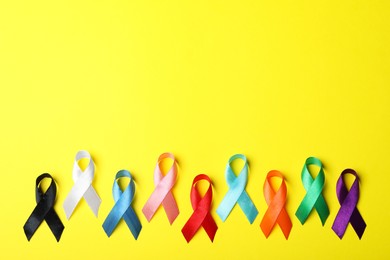 Photo of Colorful ribbons on yellow background, flat lay with space for text. World Cancer Day