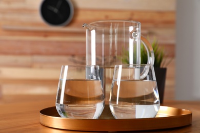 Tray with jug and glasses of water on wooden table in room. Refreshing drink