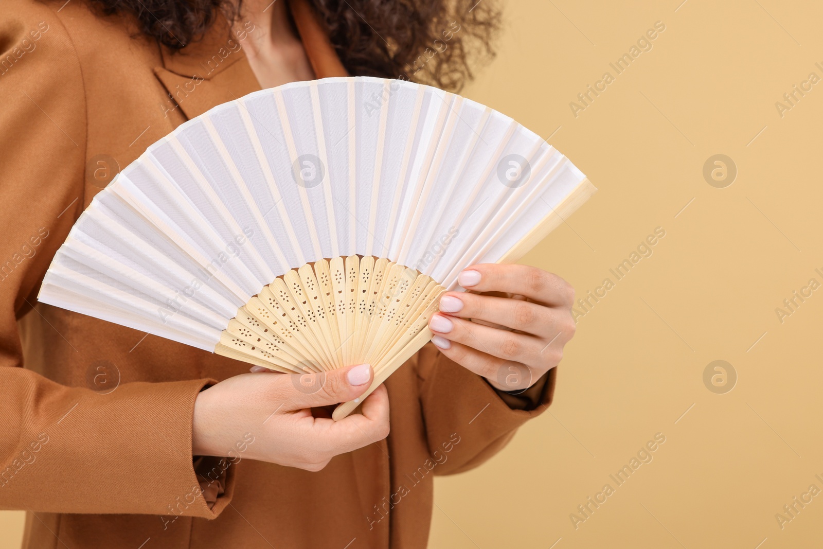 Photo of Woman holding hand fan on beige background, closeup. Space for text