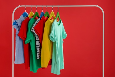Rack with stylish children clothes on red background