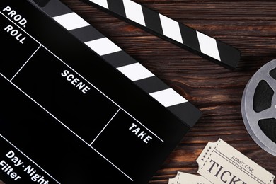 Clapperboard, movie tickets and film reel on wooden table, flat lay