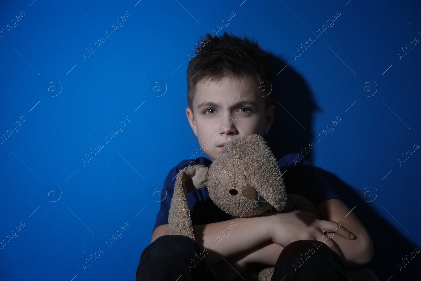 Photo of Sad little boy with toy near blue wall. Domestic violence concept