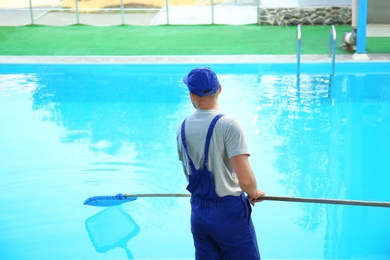 Photo of Male worker cleaning outdoor pool with scoop net