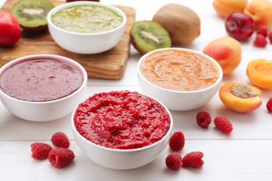 Photo of Different puree in bowls and fresh fruits on white wooden table
