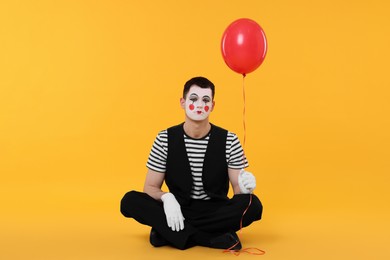 Photo of Funny mime artist with balloon on orange background