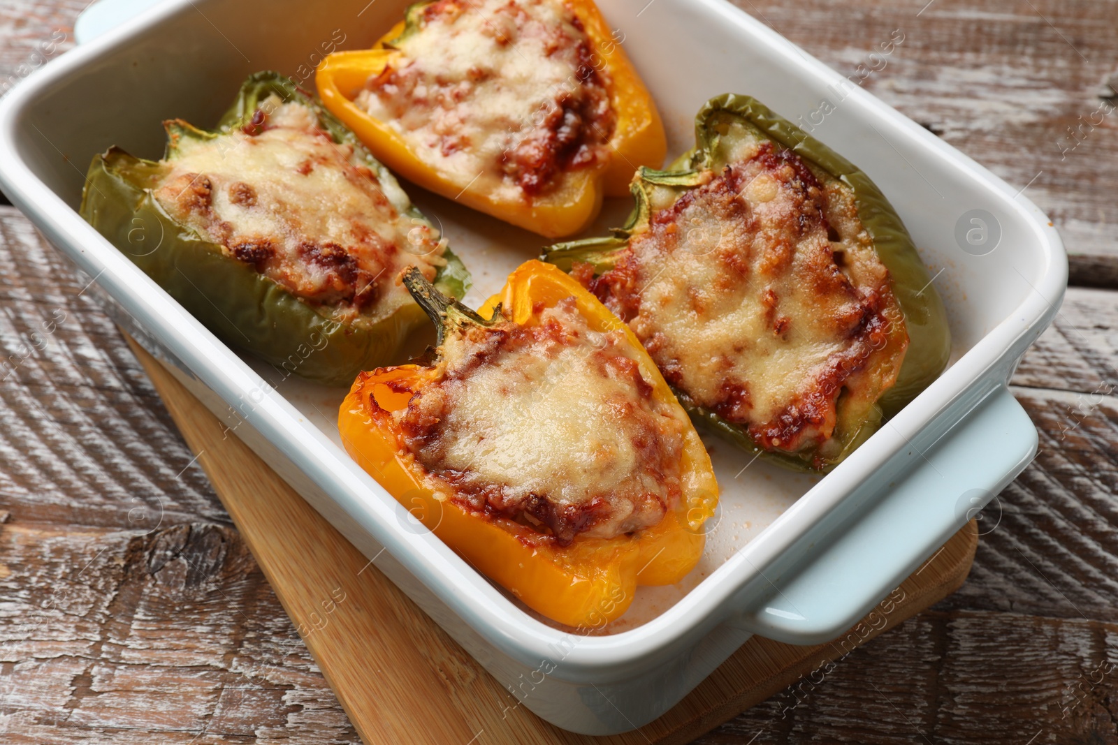 Photo of Tasty stuffed peppers in dish on wooden table, closeup