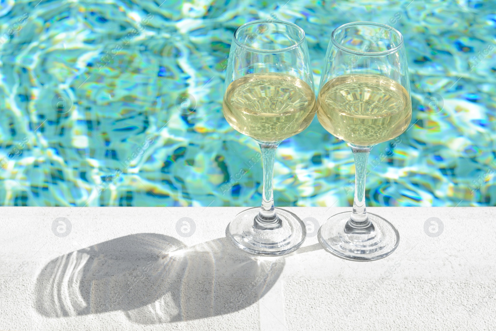 Photo of Glasses of tasty wine on swimming pool edge, space for text
