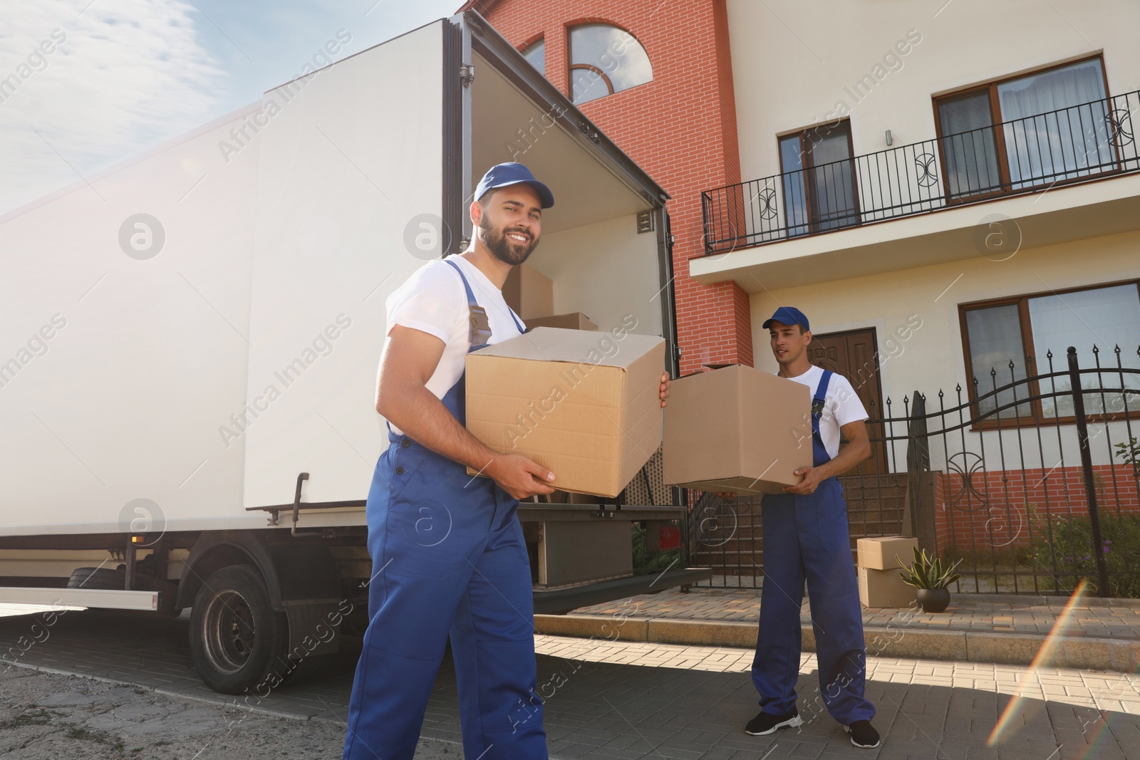 Photo of Workers unloading boxes from van outdoors. Moving service