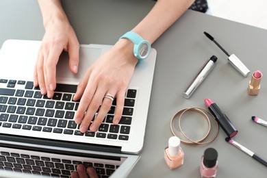 Photo of Young woman with makeup products using laptop at table. Beauty blogger