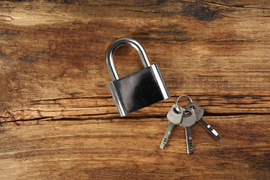 Photo of Modern padlock with keys on wooden table, flat lay