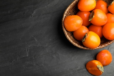 Photo of Delicious fresh persimmons on black slate table, flat lay. Space for text