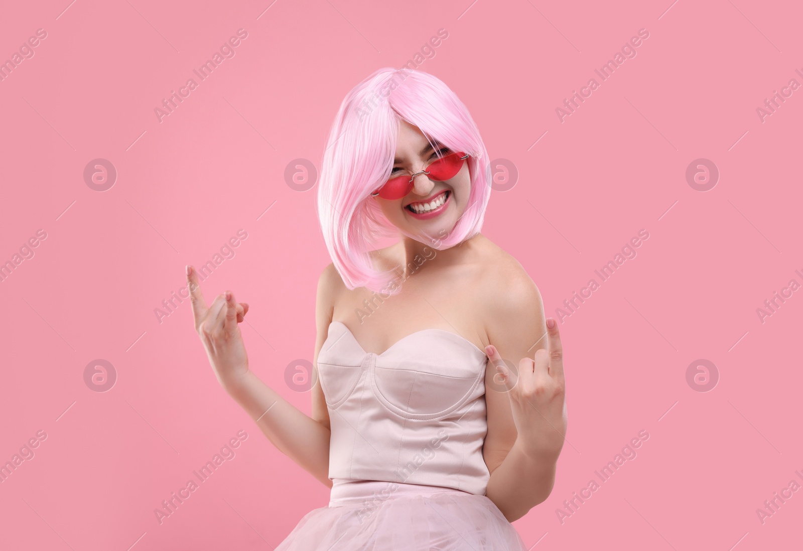 Photo of Pink look. Beautiful woman in wig and bright sunglasses showing rock sign on color background